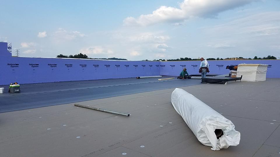 Low slope commercial roof with roofers installing new materials.